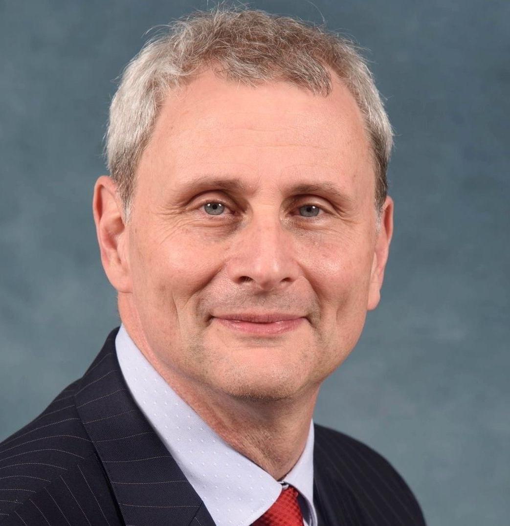 Don Leo shown from head to shoulders wearing a dark suit and red tie